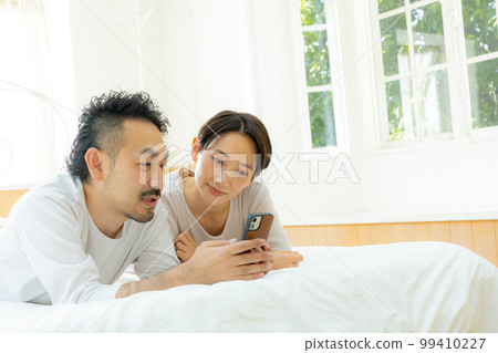 Middle couple looking at smartphone in bed Middle couple looking at smartphone in bed 99410227