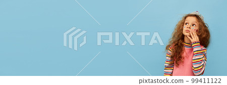 Dreamy look. Birthday look. Little cute girl, child with curly hair posing in pink dress over blue studio background. Concept of childhood, emotions, fun 99411122