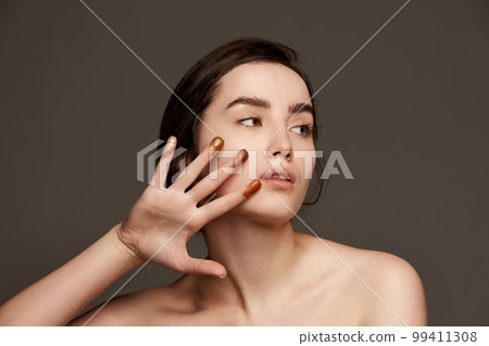 Sparkling nude eyeshadow swatches on fingers. Portrait of young beautiful girl with brown hair posing over dark grey studio background. Concept of natural beauty, skin care, cosmetology Sparkling nude eyeshadow swatches on fingers. Portrait of young beautiful girl with brown hair posing over dark grey studio background. Concept of natural beauty, skin care, cosmetology 99411308
