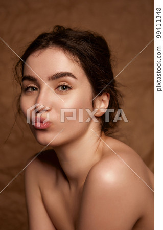 Tenderness. Beautiful young brunette girl with smooth well-kept healthy skin posing over brown studio background. Concept of natural beauty, skincare, cosmetology 99411348