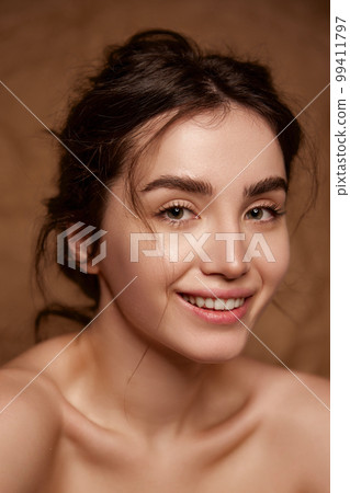Tenderness and purity. Beautiful smiling young brunette girl with clear healthy skin posing over brown studio background. Concept of natural beauty, skincare, cosmetology 99411797