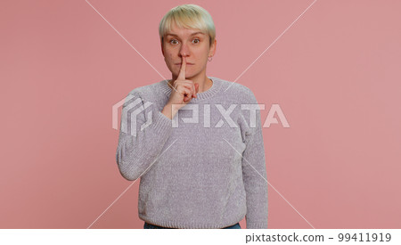 Young woman presses index finger to lips makes silence gesture sign do not tells secret shh be quiet 99411919
