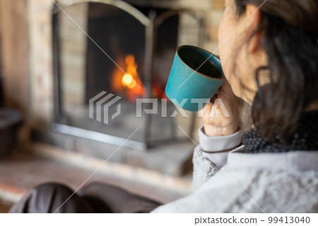 Woman's hand holding a coffee cup in front of the fireplace Woman's hand holding a coffee cup in front of the fireplace 99413040