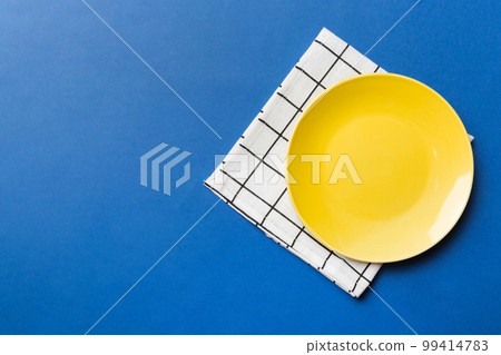 Top view on colored background empty round yellow plate on tablecloth for food. Empty dish on napkin with space for your design Top view on colored background empty round yellow plate on tablecloth for food. Empty dish on napkin with space for your design 99414783