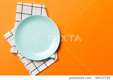 Top view on colored background empty round blue plate on tablecloth for food. Empty dish on napkin with space for your design Top view on colored background empty round blue plate on tablecloth for food. Empty dish on napkin with space for your design 99414784
