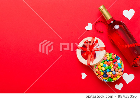 Bottle of red wine on colored background for Valentine Day with gift and chocolate. Heart shaped with gift box of chocolates top view with copy space 99415050