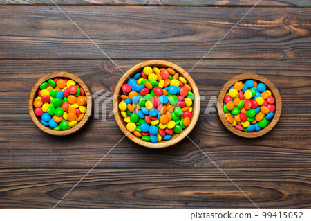 different colored round candy in bowl and jars. Top view of large variety sweets and candies with copy space different colored round candy in bowl and jars. Top view of large variety sweets and candies with copy space 99415052