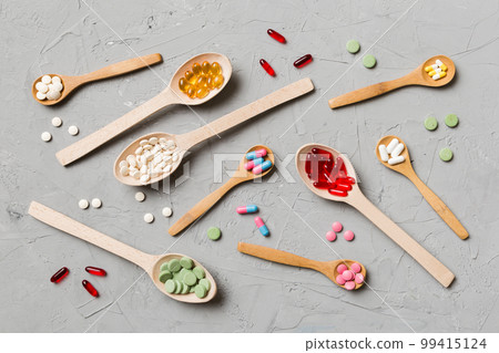 Top view Variety of vitamin and mineral pills in wooden spoon on Colored background. Top view of assorted pharmaceutical medicine pills. Dietary supplement healthcare product 99415124
