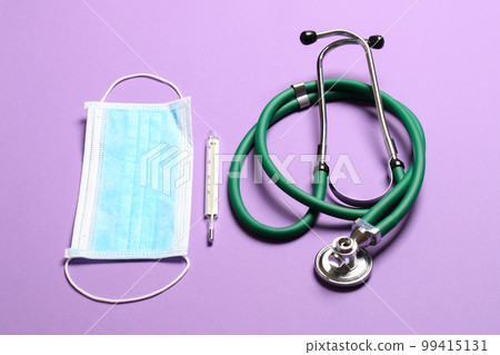 Top view of stethoscope, mercury thermometer and a protective face mask on colorful background. Medical equipment and health care concept Top view of stethoscope, mercury thermometer and a protective face mask on colorful background. Medical equipment and health care concept 99415131