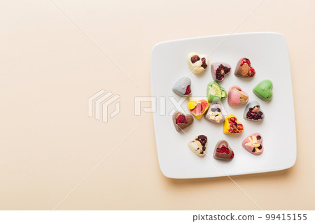 Plate with different chocolate on colored background. Assortment of fine chocolates top view vith copy space Health and obesity concept Plate with different chocolate on colored background. Assortment of fine chocolates top view vith copy space Health and obesity concept 99415155