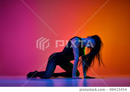 Dynamic studio shot of talented female dancer performing on stage over gradient pink orange background in neon light Dynamic studio shot of talented female dancer performing on stage over gradient pink orange background in neon light 99415454