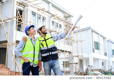 Construction engineer and architect with blueprint point to the construction site. They are in safety vests with helmets for safety. Construction engineer and architect with blueprint point to the construction site. They are in safety vests with helmets for safety. 99415982