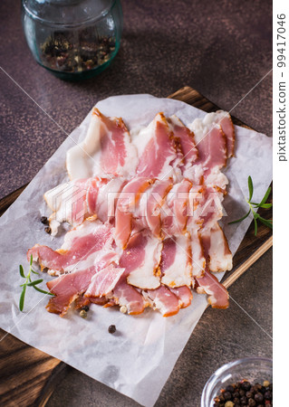 Raw bacon slices on paper on a cutting board on the table. Hearty snack. Vertical view 99417046