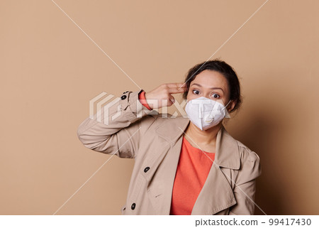 Unhappy multi-ethnic confident business woman in medical mask, makes suicide gesture, tired of everything, shoots in temple with hand, isolated against beige background. Copy advertising space Unhappy multi-ethnic confident business woman in medical mask, makes suicide gesture, tired of everything, shoots in temple with hand, isolated against beige background. Copy advertising space 99417430