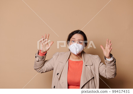 Shocked middle-aged multi-ethnic woman in medical mask, gesturing, expressing stupefaction looking at camera, isolated beige background. Quarantine, self isolation, social distance concept. Copy space Shocked middle-aged multi-ethnic woman in medical mask, gesturing, expressing stupefaction looking at camera, isolated beige background. Quarantine, self isolation, social distance concept. Copy space 99417431