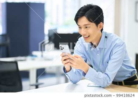 A young male businessman in plain clothes with a smartphone working in the office 99418624