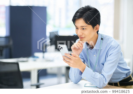一位穿著便衣、拿著智能手機在辦公室工作的年輕男性商人 99418625