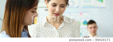 Two beautiful businesswoman discussing business document standing in office 99420171
