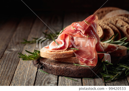 Prosciutto with bread and rosemary on an old wooden table. 99420533