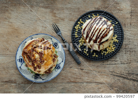 Two Homemade Soft Chocolate Buns, Cinnamon roll topped with rich cream cheese frosting and Caramel Pecanbon topped with caramel frosting and pecans served with Metal fork on old rustic wooden 99420597
