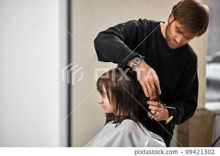 Professional male hairdresser cutting female hair in salon 99421302