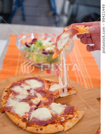 Men's hand is taking piece of pizza on wood background Men's hand is taking piece of pizza on wood background 99421449