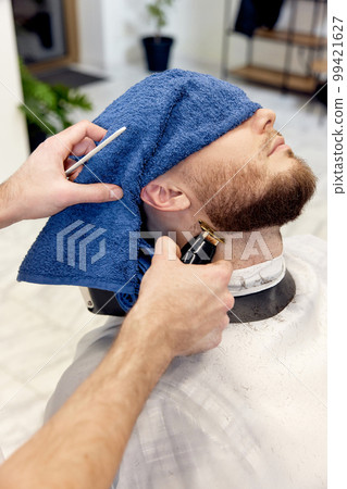 Barber shaving bearded man in barber shop. 99421627