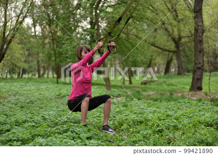 Beautiful young woman doing TRX exercise with suspension trainer sling in the outdoors Beautiful young woman doing TRX exercise with suspension trainer sling in the outdoors 99421890