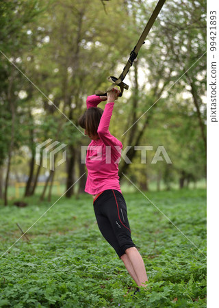 Young attractive woman does body stretching with trx fitness straps 99421893