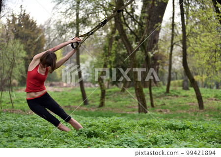 Young attractive woman does body stretching with trx fitness straps Young attractive woman does body stretching with trx fitness straps 99421894