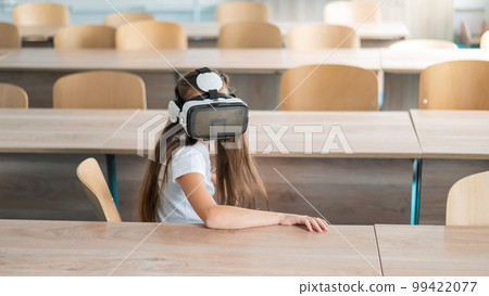 Caucasian schoolgirl wearing virtual reality glasses in the classroom.  99422077