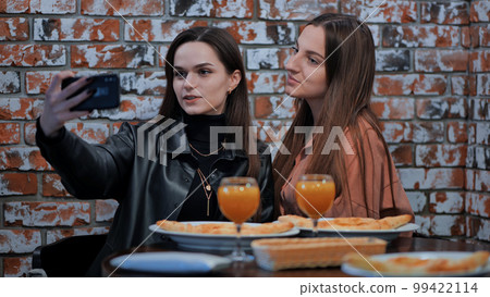 Two girls are sitting in a cafe and taking a selfie on the phone. Two girls are sitting in a cafe and taking a selfie on the phone. 99422114