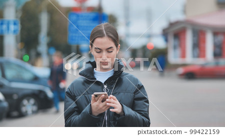 A girl walks through town and looks through her phone. 99422159