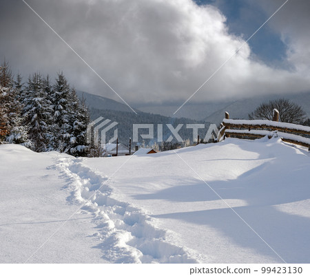 Countryside hills, groves and farmlands in winter remote alpine mountain village. Freshly trodden hiking trail path. Countryside hills, groves and farmlands in winter remote alpine mountain village. Freshly trodden hiking trail path. 99423130
