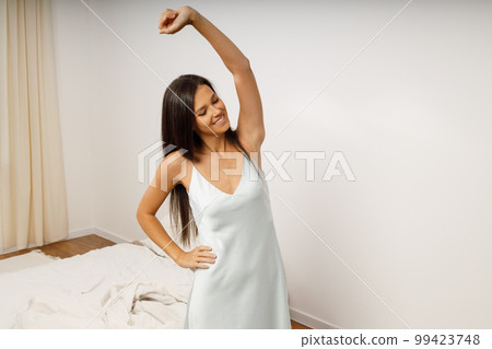 Woman in nightie stretching to warm up at morning bedroom after sleep Woman in nightie stretching to warm up at morning bedroom after sleep 99423748