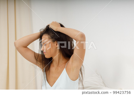 Female girl with hangover headache, time to get up for work. Beautiful young woman, dressed in silk negligee of delicate blue color, is sitting in cozy bed in the bedroom, holding her head. Female girl with hangover headache, time to get up for work. Beautiful young woman, dressed in silk negligee of delicate blue color, is sitting in cozy bed in the bedroom, holding her head. 99423756
