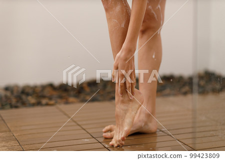 Woman under the trickles of water in pleasure shower. Girl under the spray of water. Wet legs close up Woman under the trickles of water in pleasure shower. Girl under the spray of water. Wet legs close up 99423809