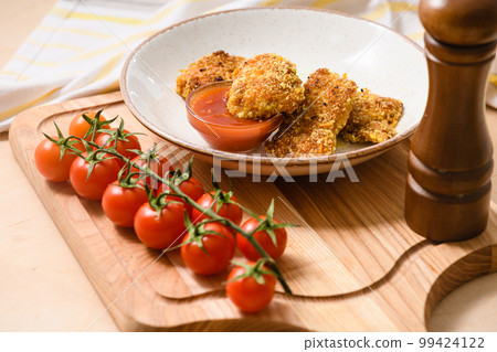Homemade chicken nuggets with cherry tomatoes and ketchup on a wooden board. 99424122