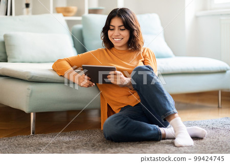 Smiling young arab woman relaxing with digital tablet at home 99424745