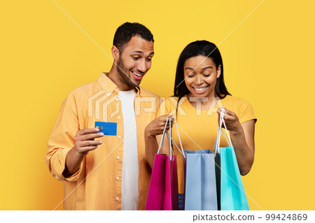 Glad shocked young african american husband and wife looking at package with purchases, using credit card Glad shocked young african american husband and wife looking at package with purchases, using credit card 99424869