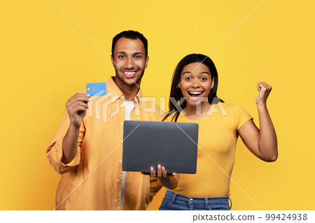 Cheerful young african american wife and husband make victory and success sign with laptop and credit card Cheerful young african american wife and husband make victory and success sign with laptop and credit card 99424938