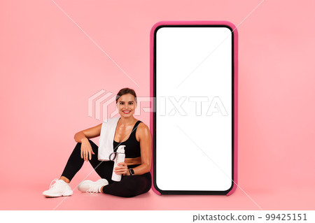 Online Offer. Smiling Sporty Woman Sitting Near Huge Blank Smartphone Online Offer. Smiling Sporty Woman Sitting Near Huge Blank Smartphone 99425151