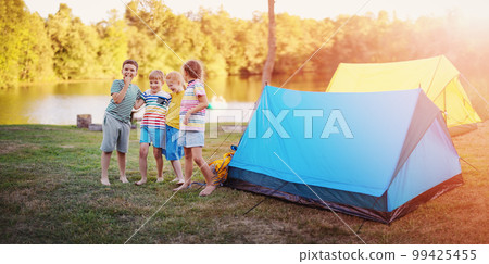 Group of four children standing near colourful tents in nature. Group of four children standing near colourful tents in nature. 99425455