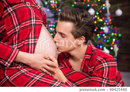 A man kneels before his wife and kisses her pregnant belly. 99425498