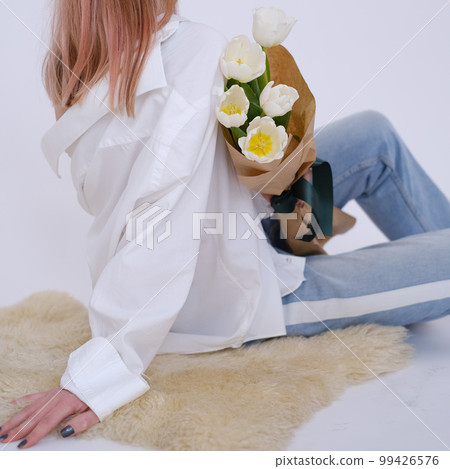 Woman in white shirt sitting and holding a bouquet of white tulips Woman in white shirt sitting and holding a bouquet of white tulips 99426576