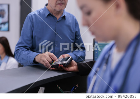 Elderly patient typing credit card pin on pos paying for medication treatment and appointment during checkup visit in hospital waiting area. Health care service support and concept Elderly patient typing credit card pin on pos paying for medication treatment and appointment during checkup visit in hospital waiting area. Health care service support and concept 99426855