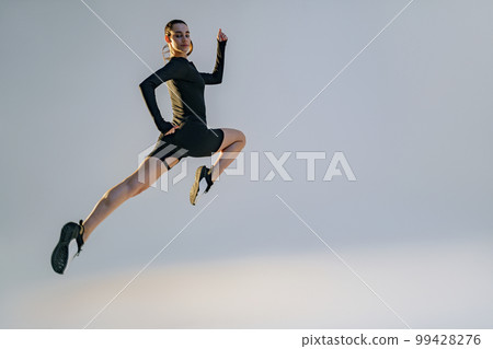 Determined sporty woman running in Mid-Air exercising during cardio workout over studio background 99428276