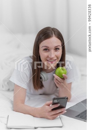 Portrait of Good Healthy woman eating green apple and resting in bed at bedroom. Lifestyle at home concept. 99428336