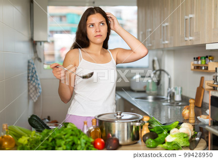 Young confused woman decides what to cook in kitchen 99428950