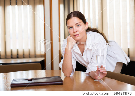 Cheerful young female with glass of champagne posing at office 99428976